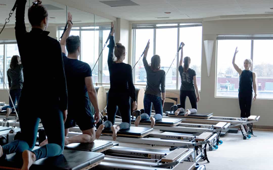 Instructor and student group on pilates reformers captioned 'Pilates Reformer Classes'